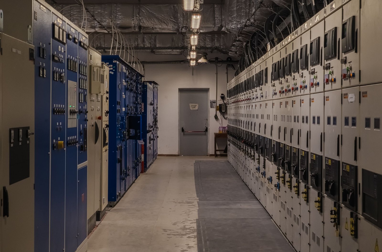 A long aisle in a commercial electrical room lined with industrial switchgear and control cabinets.